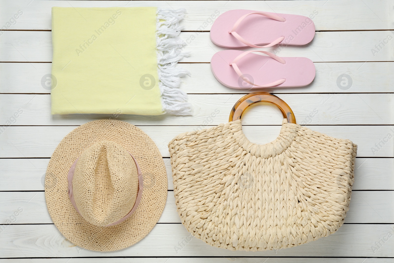 Photo of Beach bag, towel, straw hat and flip flops on white wooden background, flat lay