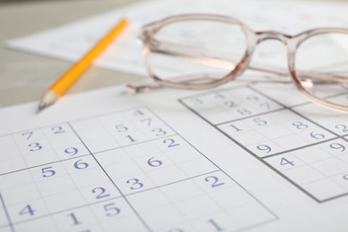 Photo of Sudoku, pencil and eyeglasses on table, closeup view