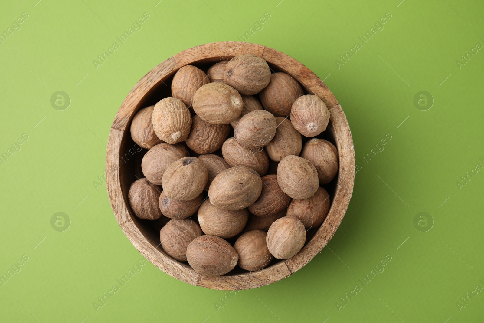 Photo of Whole nutmegs in bowl on light green background, top view