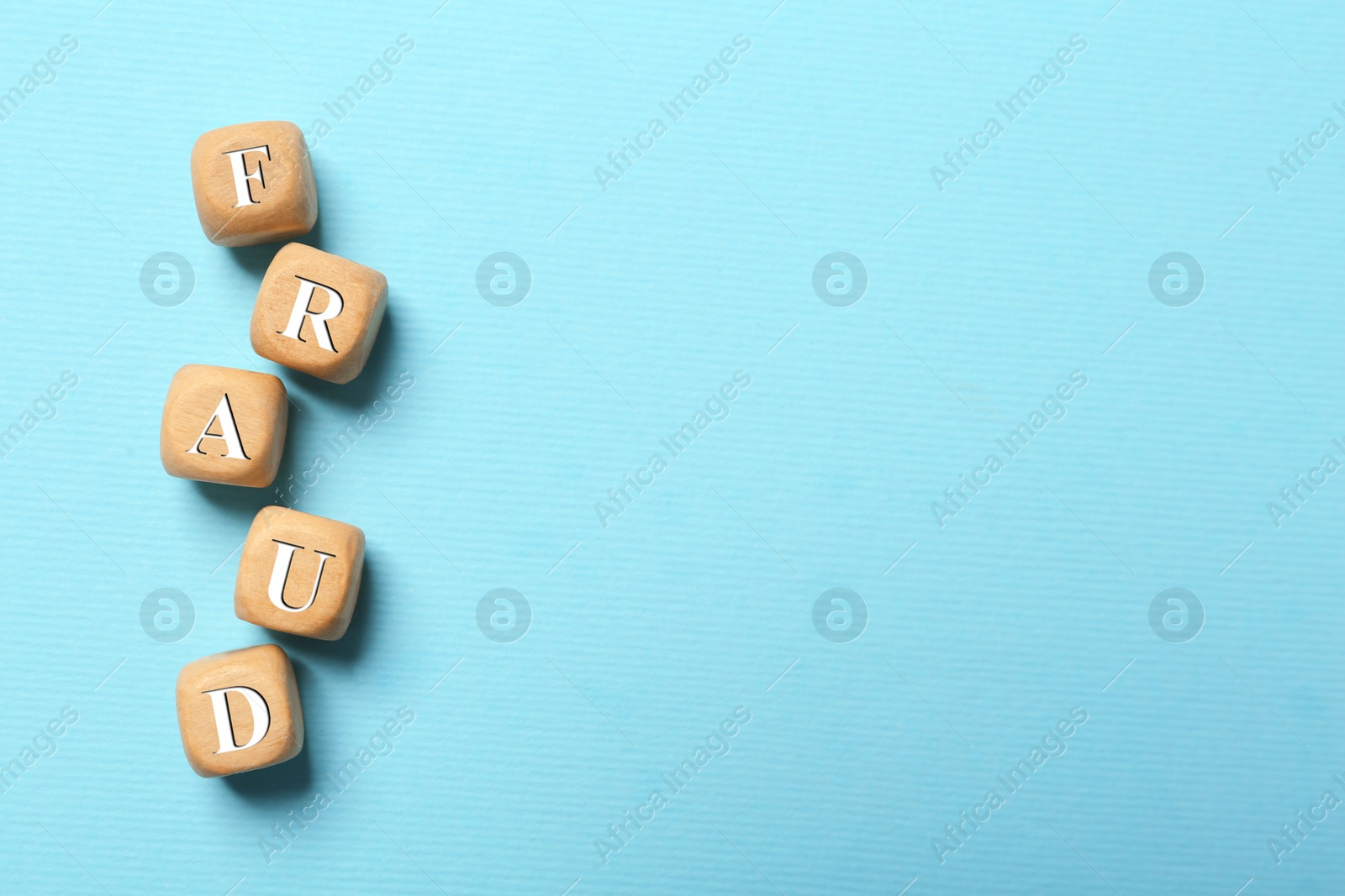 Photo of Word Fraud of wooden cubes with letters on light blue background, flat lay. Space for text