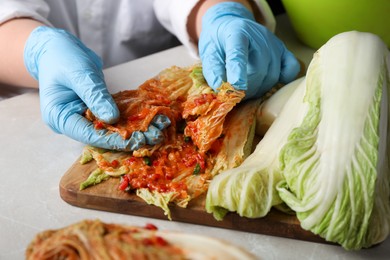 Photo of Woman preparing spicy cabbage kimchi at beige marble table, closeup