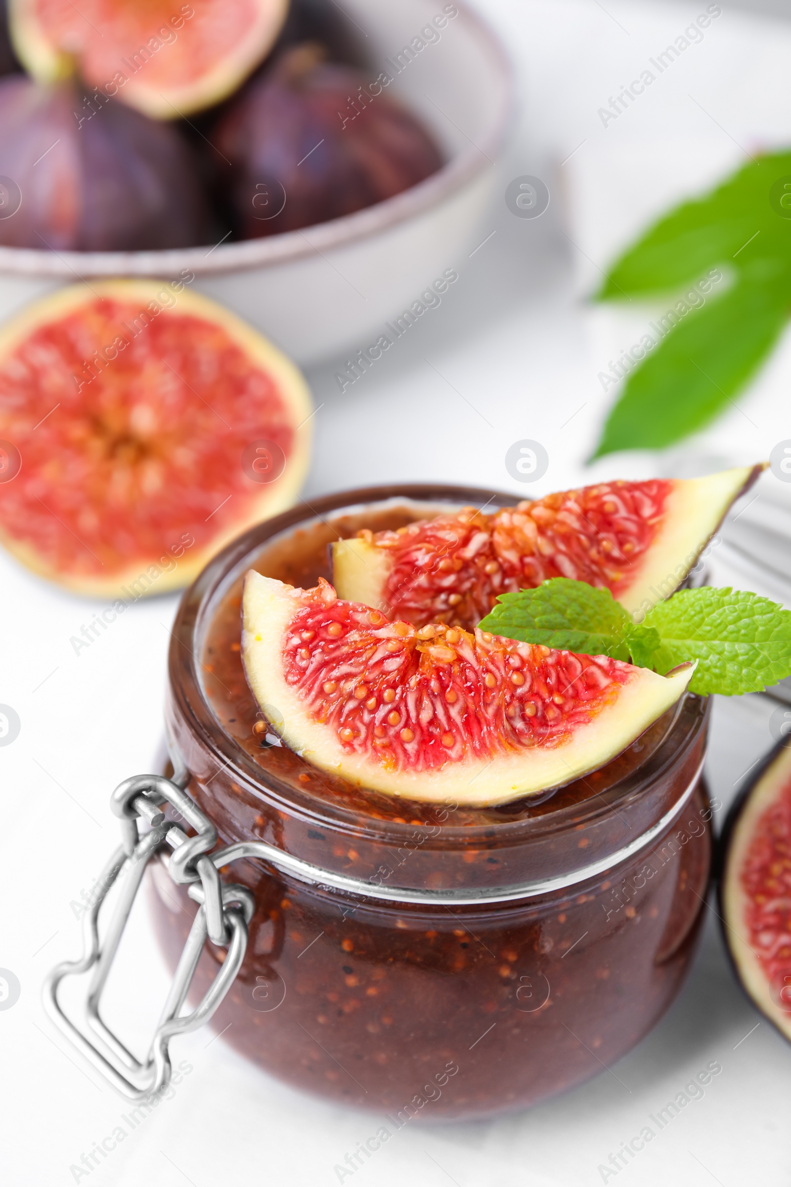 Photo of Glass jar of tasty sweet fig jam and fruits on white tiled table