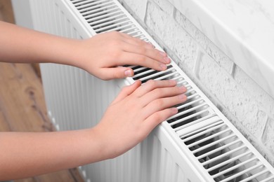 Photo of Girl warming hands on heating radiator indoors, closeup