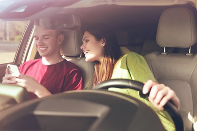 Photo of Happy young couple looking at smartphone in car