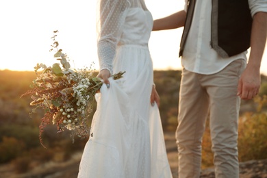Photo of Happy newlyweds with beautiful field bouquet outdoors, closeup