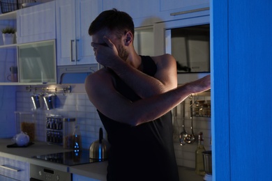 Photo of Man standing near refrigerator in kitchen at night