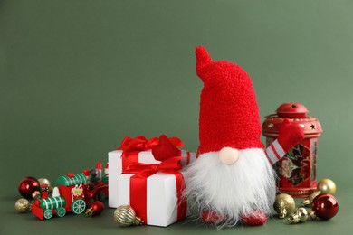 Photo of Cute Christmas gnome, gift boxes and festive decor on green background