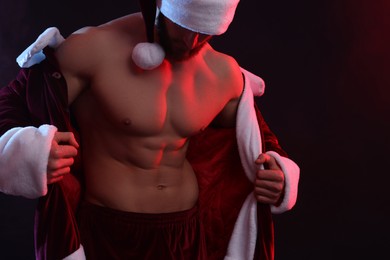 Attractive young man with muscular body in Santa costume on black background, space for text