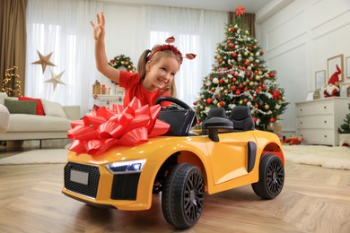 Photo of Cute little girl playing with toy car in room decorated for Christmas