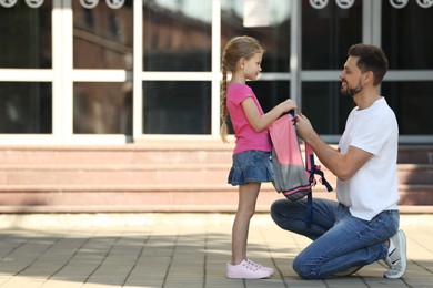 Photo of Happy father preparing his daughter to school outdoors. Space for text
