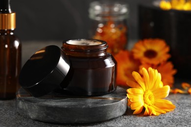 Photo of Jar of cream and beautiful calendula flowers on grey table, closeup