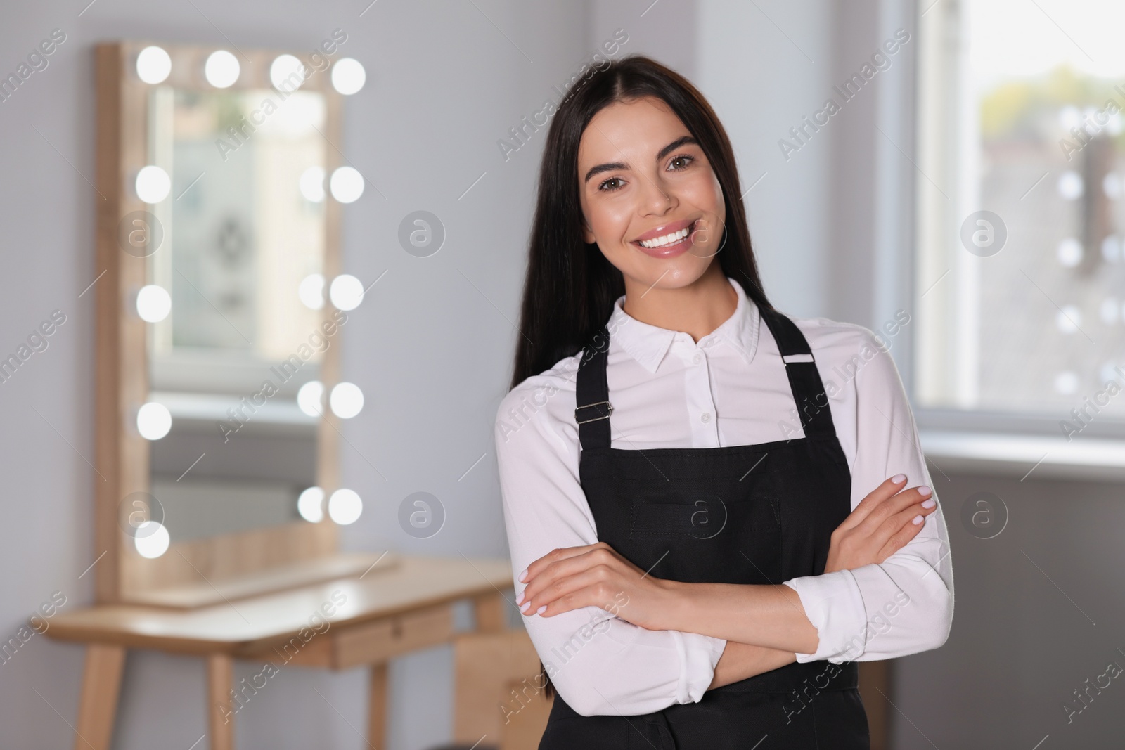 Photo of Portrait of professional hairdresser wearing black apron in beauty salon, space for text