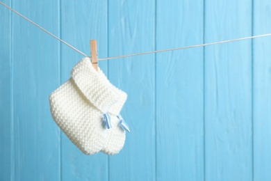 Photo of Baby booties on laundry line against color wooden background, space for text. Child accessories