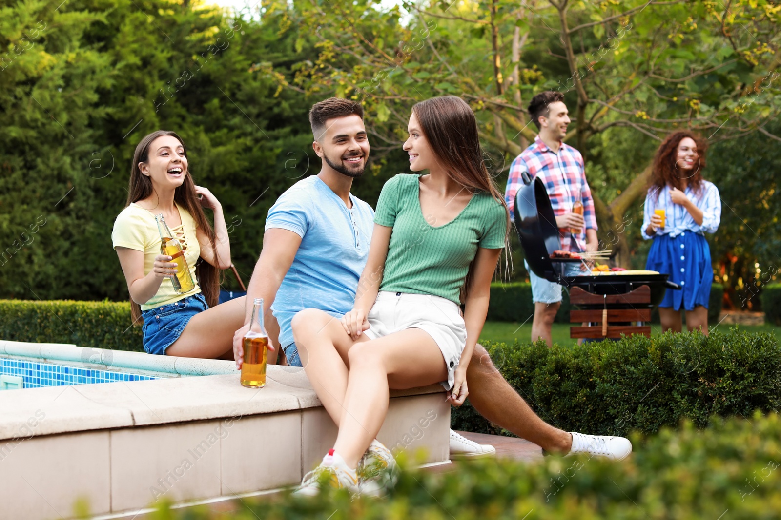 Photo of Happy friends with drinks at barbecue party near swimming pool outdoors