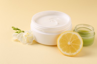 Photo of Moisturizing cream in open jars, lemon and freesia flower on beige background. Body care products