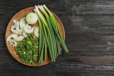 Photo of Wooden plate with cut onion leaves and bulbs on dark wooden table, top view. Space for text