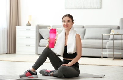 Photo of Athletic young woman with protein shake on floor at home