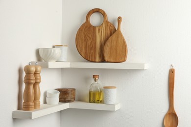 Wooden cutting boards, dishware and kitchen utensils on white shelves