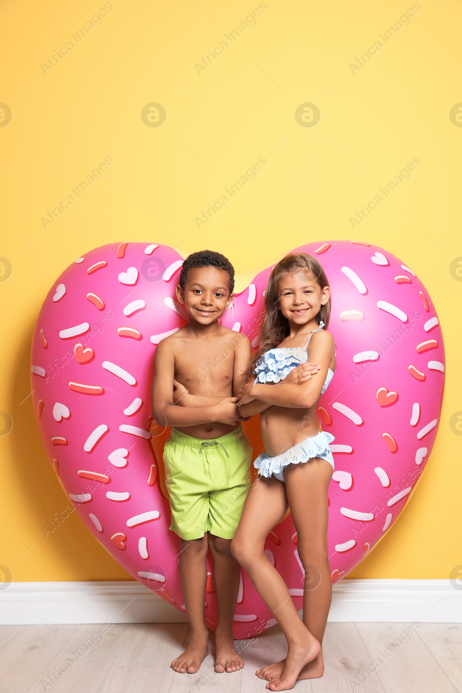Photo of Cute little children with bright heart shaped inflatable ring near color wall