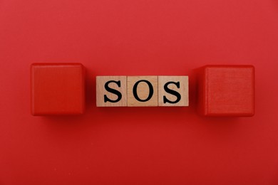 Photo of Abbreviation SOS made of wooden cubes on red background, flat lay