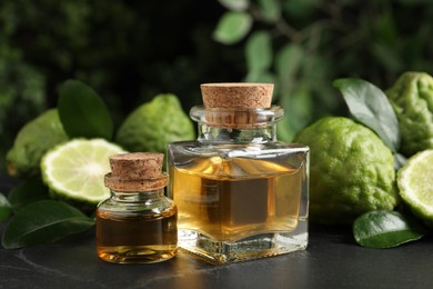 Photo of Glass bottles of bergamot essential oil and fresh fruits on black stone table