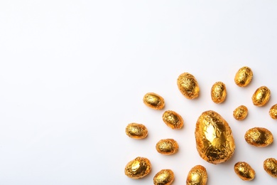 Photo of Chocolate eggs wrapped in golden foil on white background, flat lay. Space for text