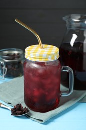 Delicious iced hibiscus tea and dry flowers on light blue wooden table