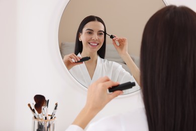 Photo of Beautiful young woman applying mascara near mirror indoors. Space for text