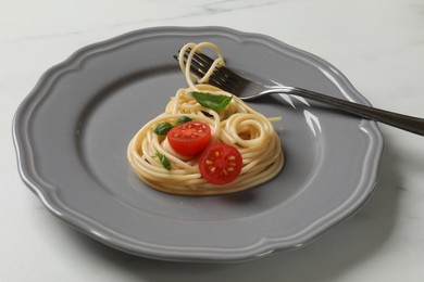 Photo of Heart made of tasty spaghetti, fork, tomato and basil on white marble table