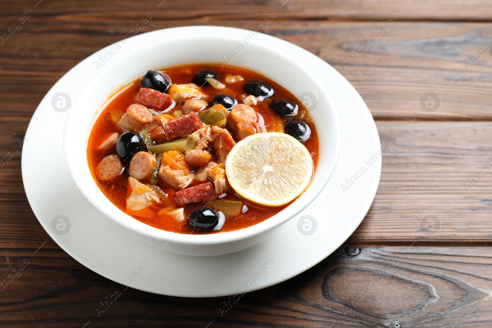 Photo of Meat solyanka soup with sausages, olives and vegetables on wooden table, space for text