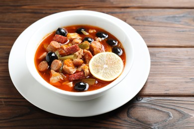 Meat solyanka soup with sausages, olives and vegetables on wooden table, space for text