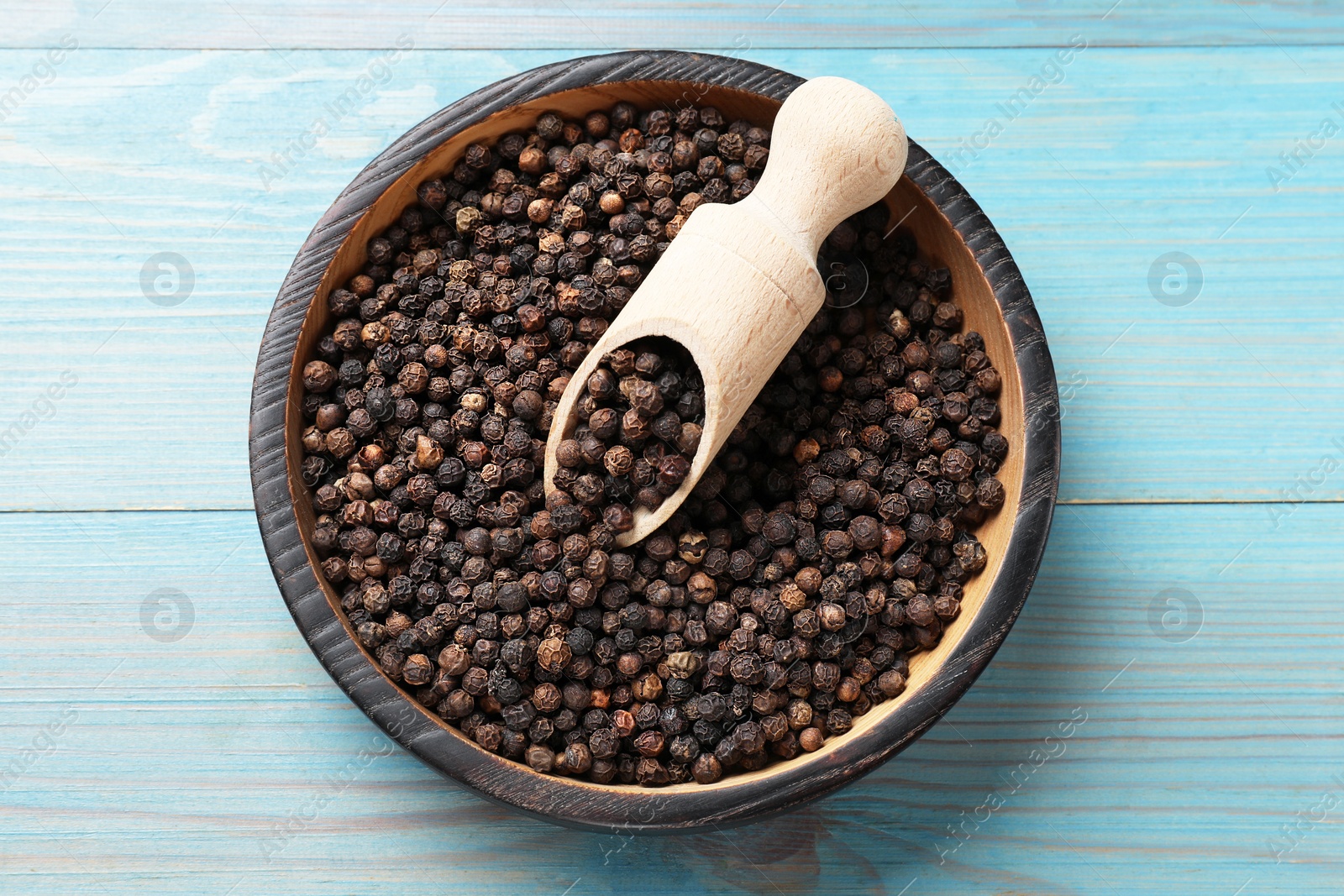 Photo of Aromatic spice. Black pepper in bowl and scoop on light blue wooden table, top view