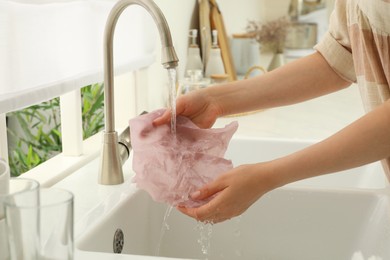 Woman washing beeswax food wrap under tap water in kitchen sink, closeup