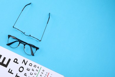 Vision test chart and glasses on light blue background, flat lay. Space for text