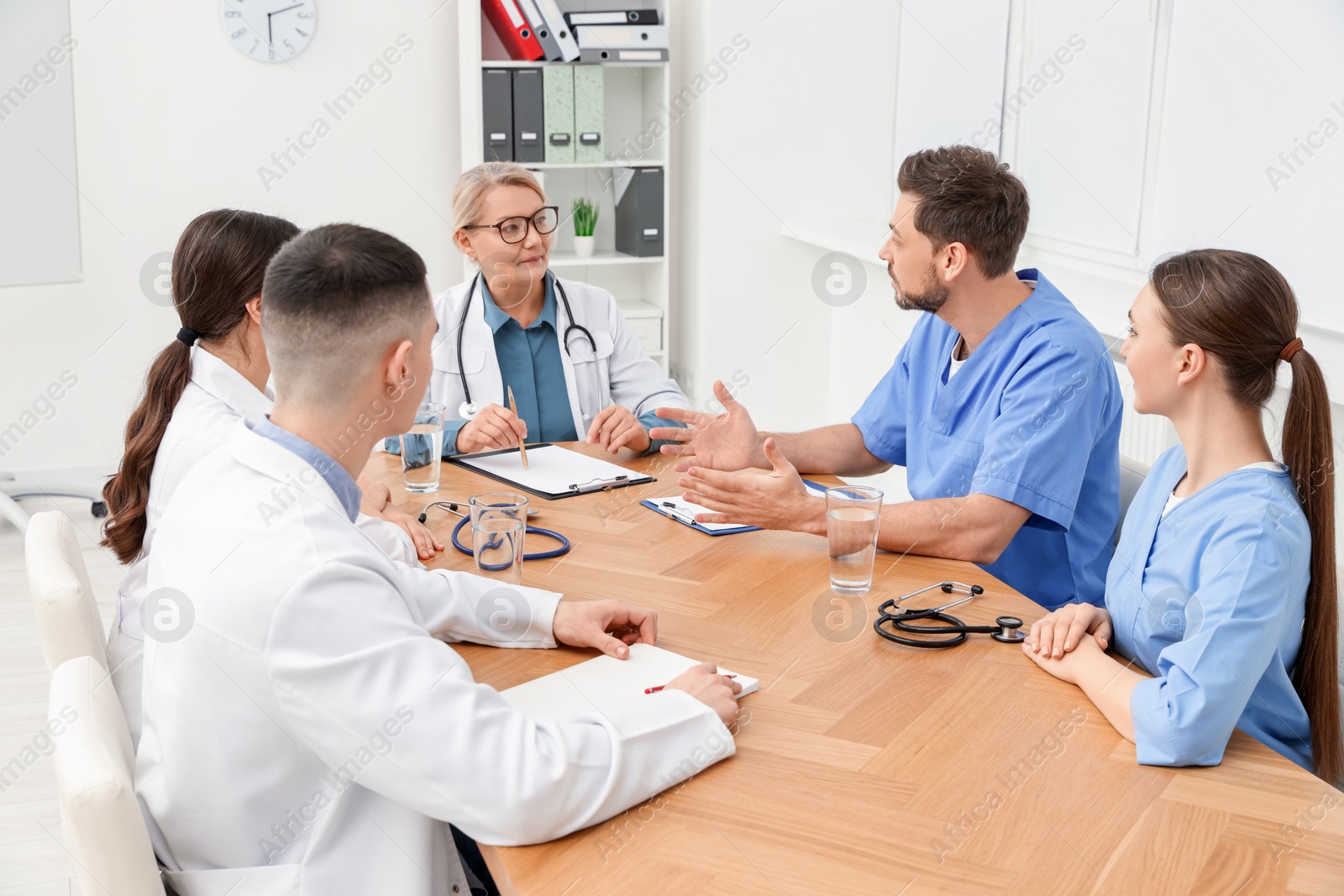 Photo of Medical conference. Team of doctors having discussion with speaker at wooden table in clinic