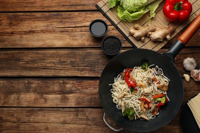 Stir fried noodles with chicken and vegetables in wok on wooden table, flat lay. Space for text
