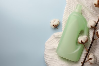 Photo of Bottle of fabric softener, white knitted cloth and cotton flowers on light background, flat lay. Space for text