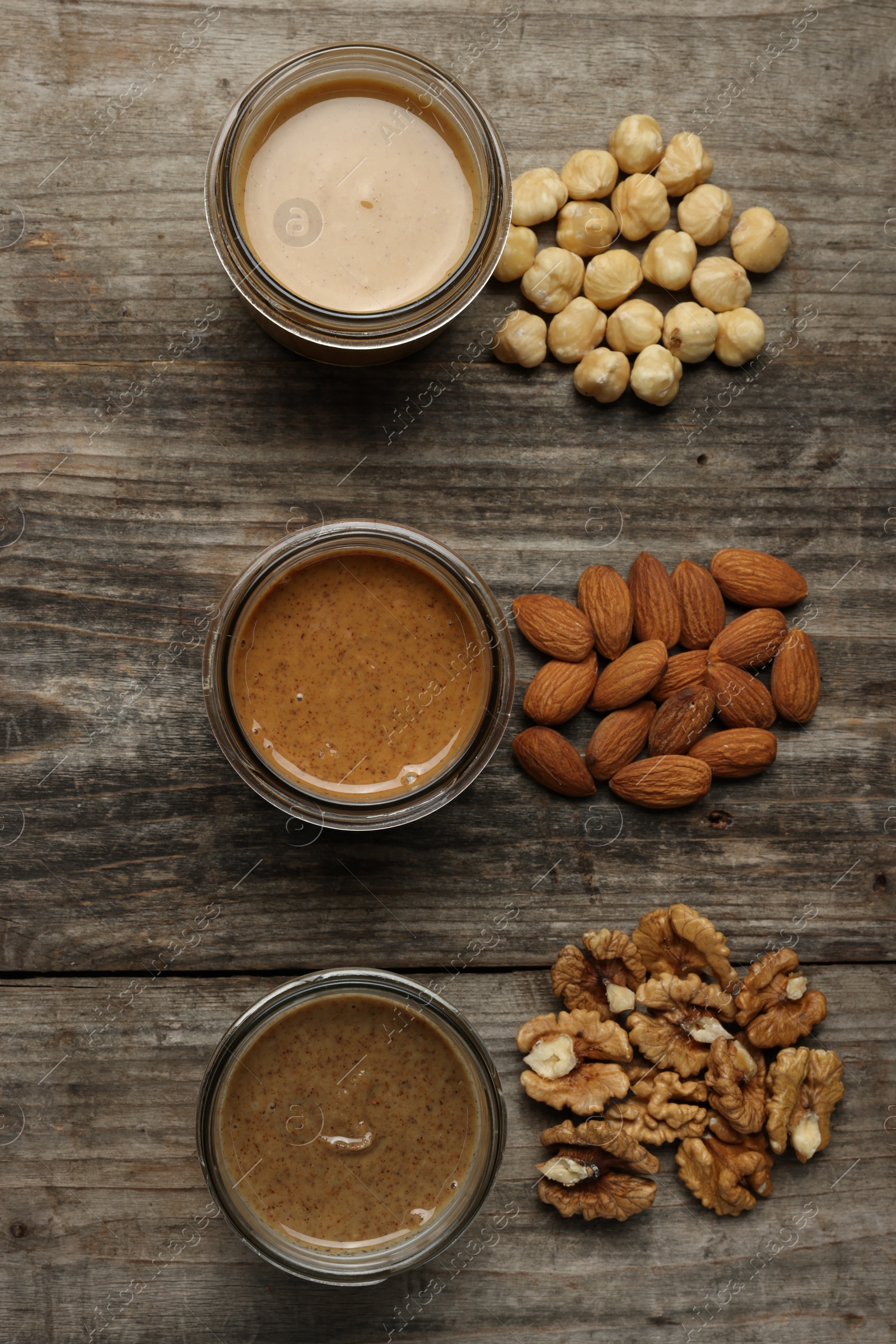 Photo of Tasty nut butters in jars and raw nuts on wooden table, flat lay