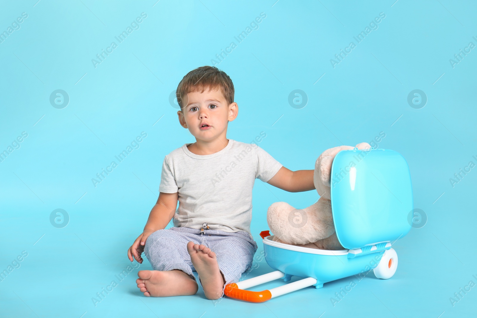 Photo of Cute little boy with toy and suitcase on blue background