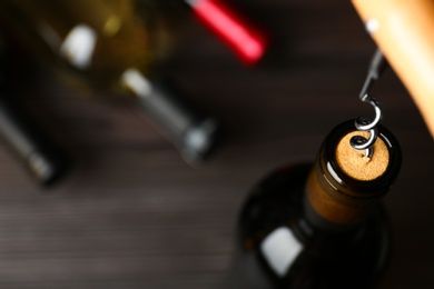 Photo of Bottle of wine and corkscrew on blurred background, space for text