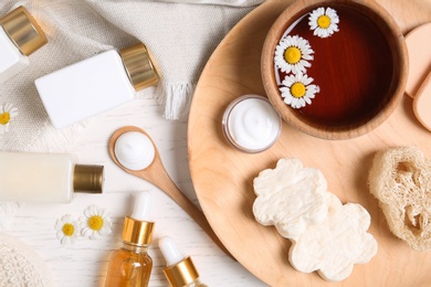 Flat lay composition with different cosmetic products and chamomile flowers on white table