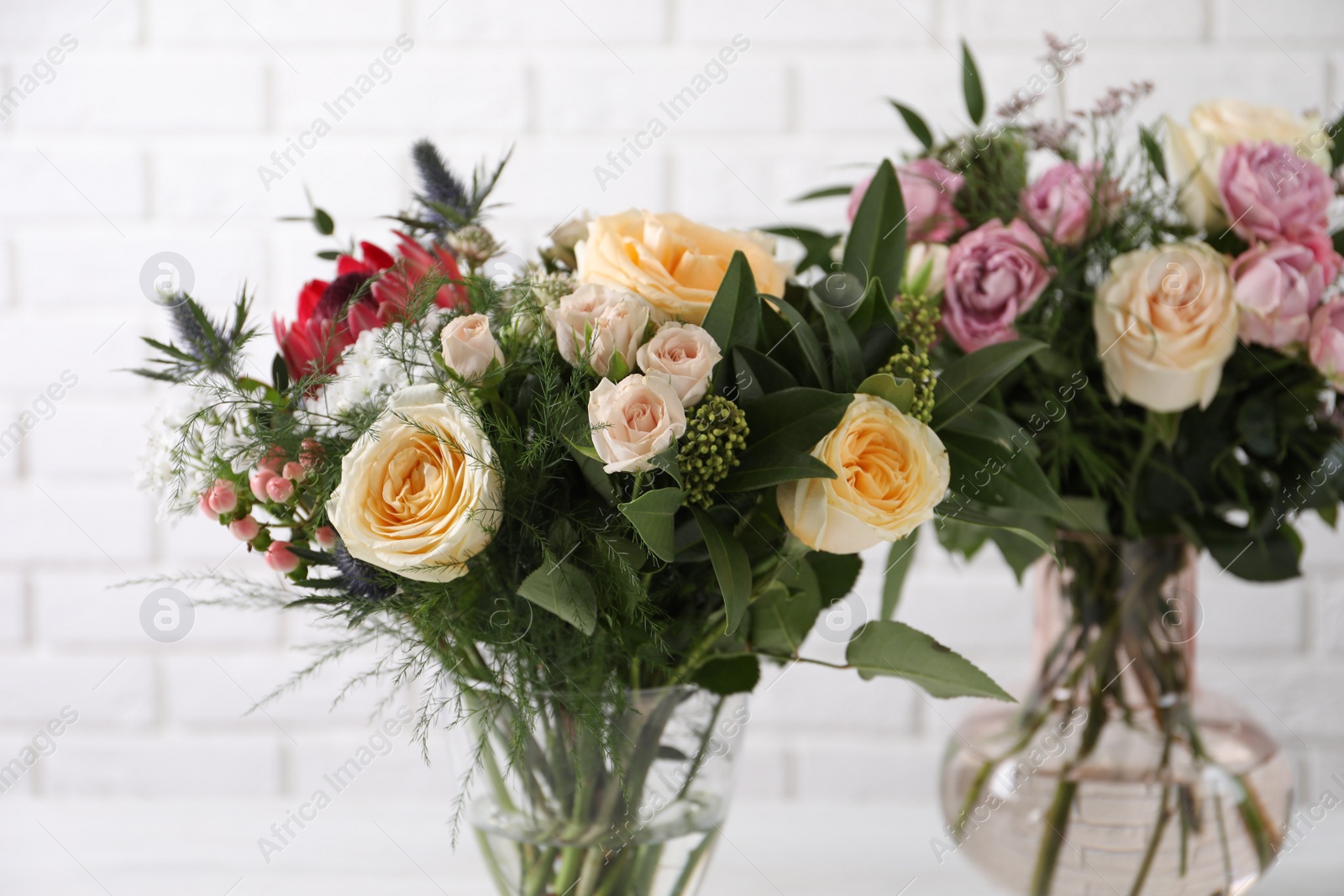 Photo of Beautiful bouquets with fresh flowers against white brick wall, closeup