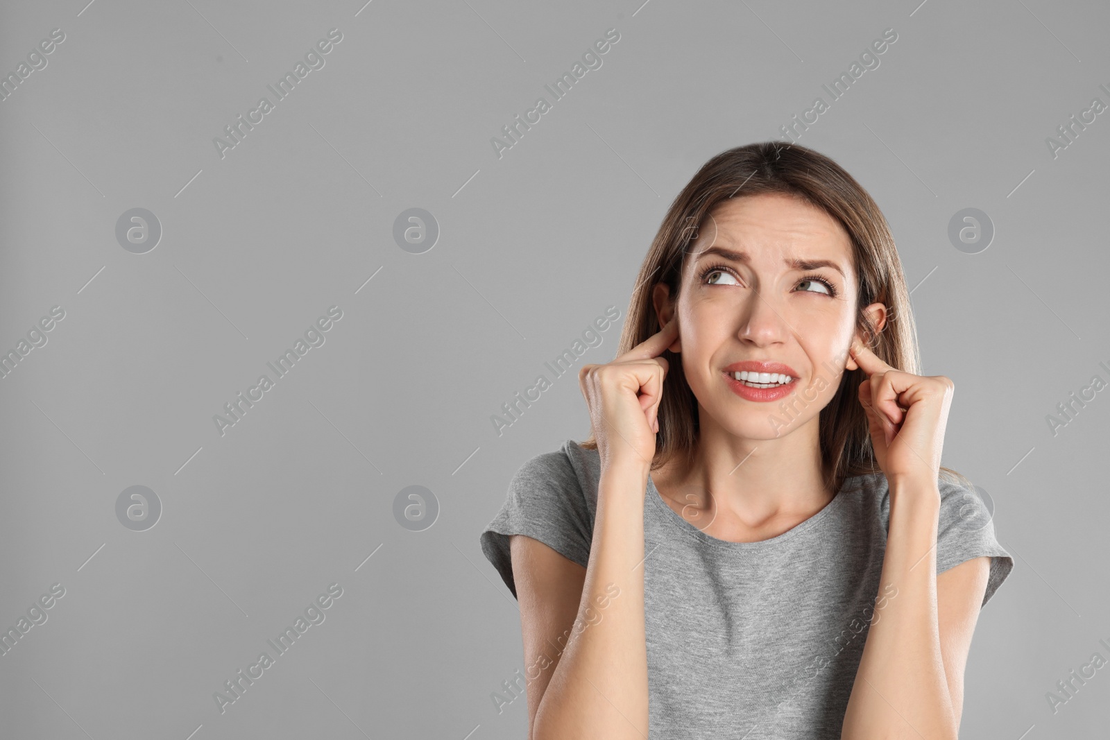 Photo of Emotional young woman covering her ears with fingers on grey background. Space for text