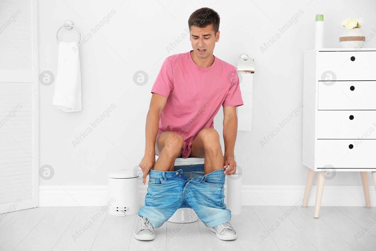 Photo of Young man suffering from diarrhea on toilet bowl at home