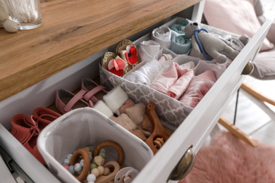 Photo of Modern open chest of drawers with baby clothes and accessories in room, closeup