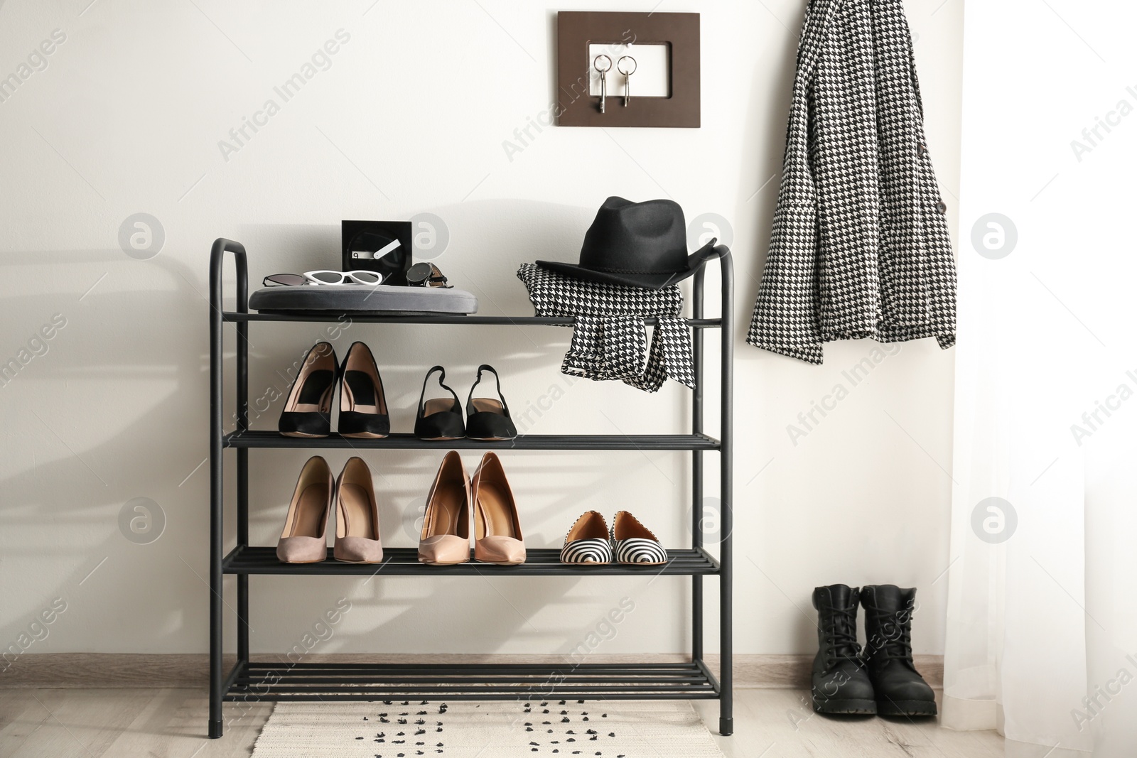 Photo of Black shelving unit with shoes and different accessories near white wall in hall