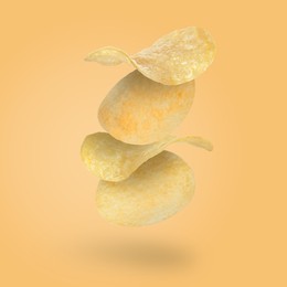 Tasty potato chips falling on pale light orange background