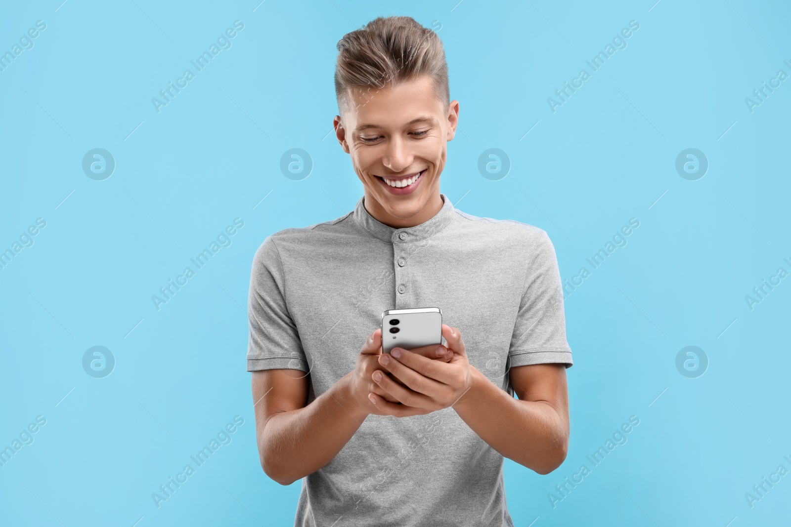 Photo of Happy young man sending message via smartphone on light blue background
