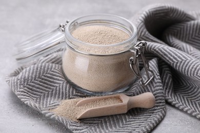 Photo of Glass jar and scoop with active dry yeast on light grey table, closeup