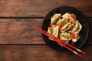 Photo of Delicious gyoza (asian dumplings) with sesame seeds, green onions, chili peppers and chopsticks on wooden table, top view. Space for text